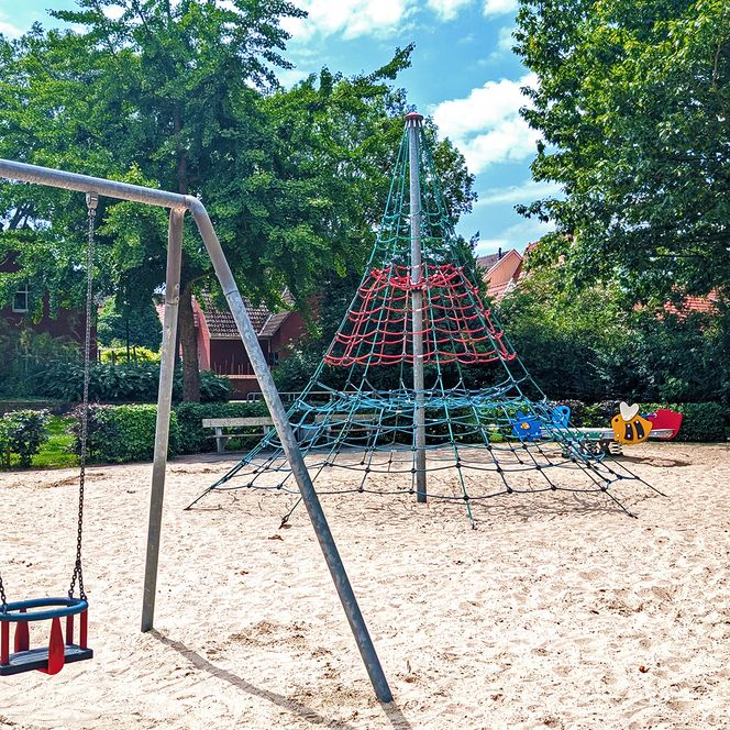 Kleinkind-Schaukel und andere Spiel- und Klettergeräte im Hintergrund.