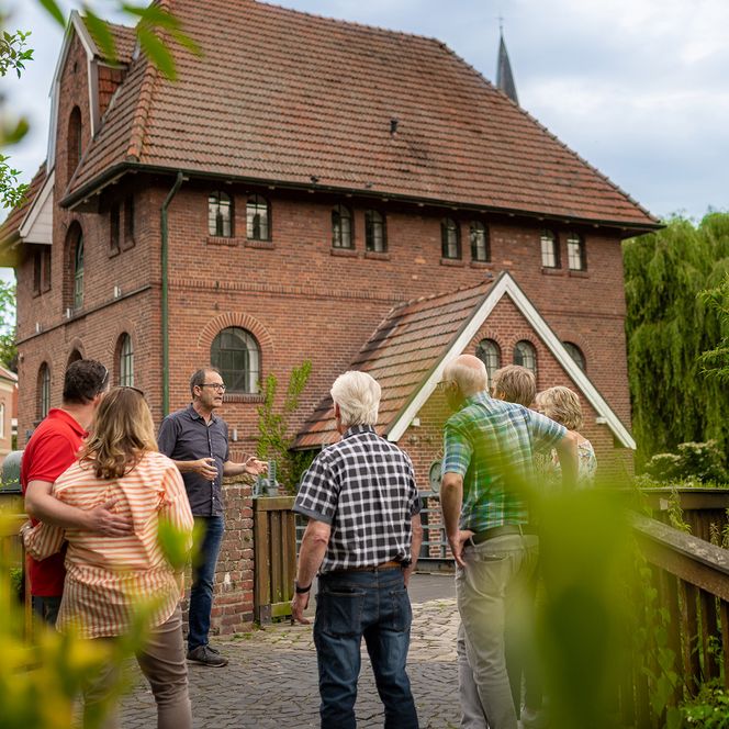 Eine Gruppe Menschen lauscht gespannt den Geschichten des Stadtführers vor deer alten Mühle in Schüttorf.