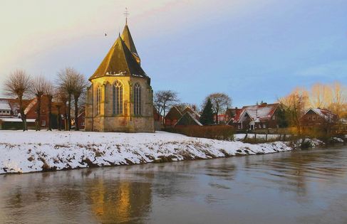 Blick vom Fluss her auf die evangelisch reformierte Kirche in Ohne. Es ist Winter und vor der Kirche liegt Schnee bei blauen Himmel und Sonnenschein