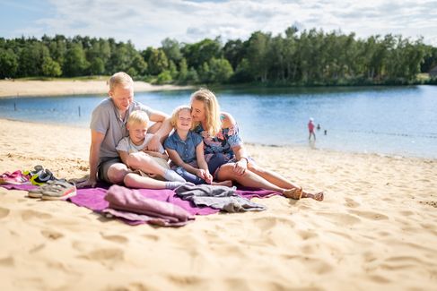 Eltern mit zwei Kindern sitzen gemütlich in der Sonne am Strand vom Quendorfer See.