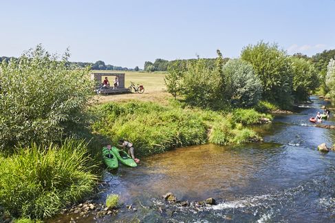 Das Vechtefenster Isterberg bietet einen wunderschönen Platz zum Picknicken mit Blick auf die Vechte. Die Sonne scheint und auf der Vechte sind Kanufahrer unterwegs.